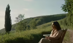 a woman in an evening dress seated on a chair overlooking a path