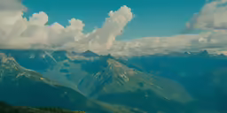 clouds fill the sky over mountains as a man stands on top of a mountain