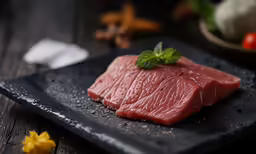 a plate of raw tuna on a black square surface