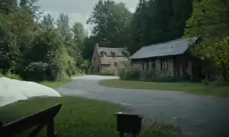an old farm house on a rural road with two benches in front of it