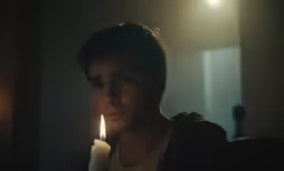 a woman looks into the distance as she holds a candle in her hand