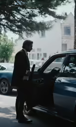 a man in a business suit leaning against his car
