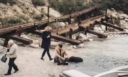 three people standing on a shoreline next to a body of water