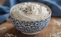 a bowl of whipped cream sits on a wooden table