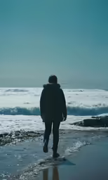 a man walking on the shore line towards the ocean