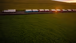 a bunch of cars in the distance going by with a field,a line up of cargo trains travelling down a track