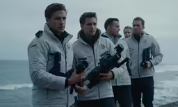 a group of men standing on the beach holding camera equipment