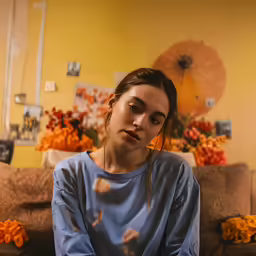 a woman is seated on a couch with orange flowers