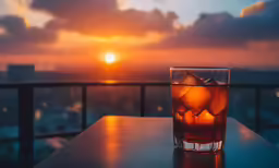 glass full of ice water and drink on wooden table at sunset