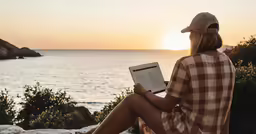 woman sitting on top of a rock, holding a book