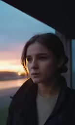 a young woman is standing by the water at sunset