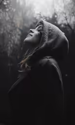 a woman wearing a hoodie standing in front of a forest