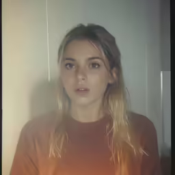 woman in an orange top and hair color looking directly