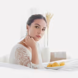 a woman is sitting on the bed with a plate of fruit in her hand