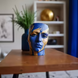 a blue and gold mask sitting on a table in front of a plant