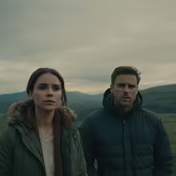 two people standing on top of a hill, one holding a jacket