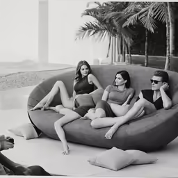three people laying on top of a couch in front of a palm tree