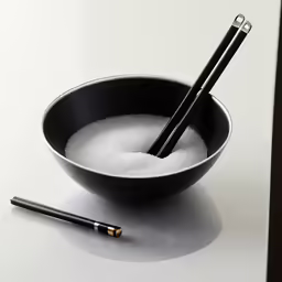a black bowl filled with salt and two black chopsticks on a white table