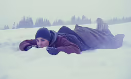 a girl lying in the snow near trees