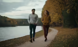 a man and woman walk down a path next to a river