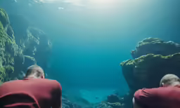 two guys diving in the water, with the sunlight shining over them