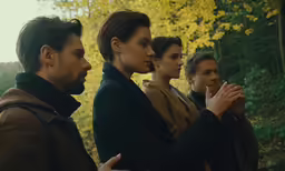 four people stand in front of trees and look at something