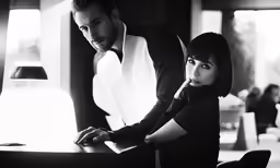 a man standing next to a woman sitting at a table