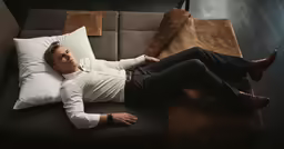 man lying on a couch with his foot propped up on a pillow