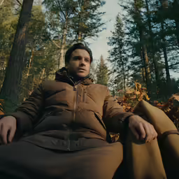 a man in a jacket and coat sitting on the ground