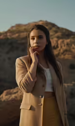 a woman in a tan jacket stands and poses for the camera