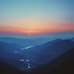 some hills are shown during sunset with a sun setting in the distance