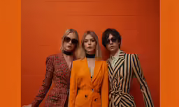 three women standing next to each other in front of an orange brick wall