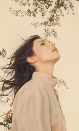 a woman in white stands under a tree looking up at something