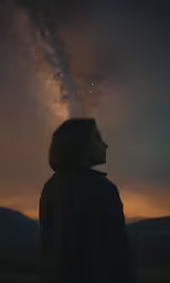 a person standing in the wilderness looking at the sky with stars