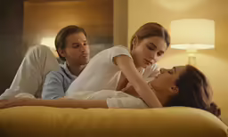two people sitting in bed with an adult standing next to them