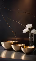 white flowers are in brass bowls on a dark counter