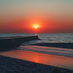 the sun rising over a body of water with a rock wall next to it