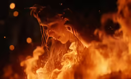 the woman has long hair and is standing by a bright fire