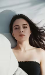 a beautiful young woman laying on a white sheet