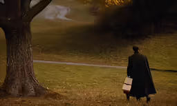 a man in black coat walking near a tree