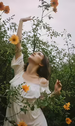 woman in a dress with her arm extended as she stands in the air with arms outstretched holding a branch that just