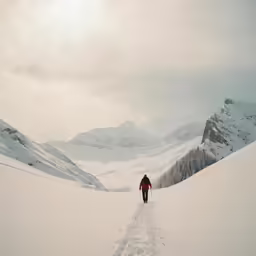 a lone person walking through the snow toward mountain ranges
