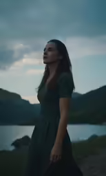 woman in a green dress standing by a lake during dusk