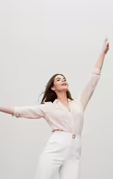 a woman is smiling and dancing on a white surface