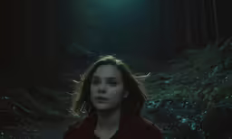 a young woman looks into the distance in a dark forest