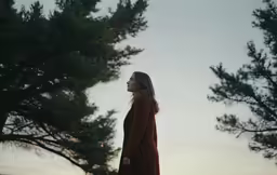 a woman standing under some trees in the sunset