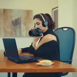 a woman sitting at a desk with a camera and laptop in front of her