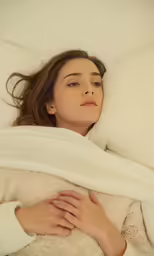 a woman lays in bed wrapped up with a blanket