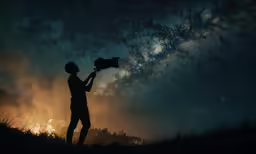 silhouetted man in field with stars at night holding large camera