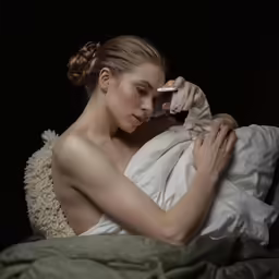 a woman is sitting on her bed using a phone